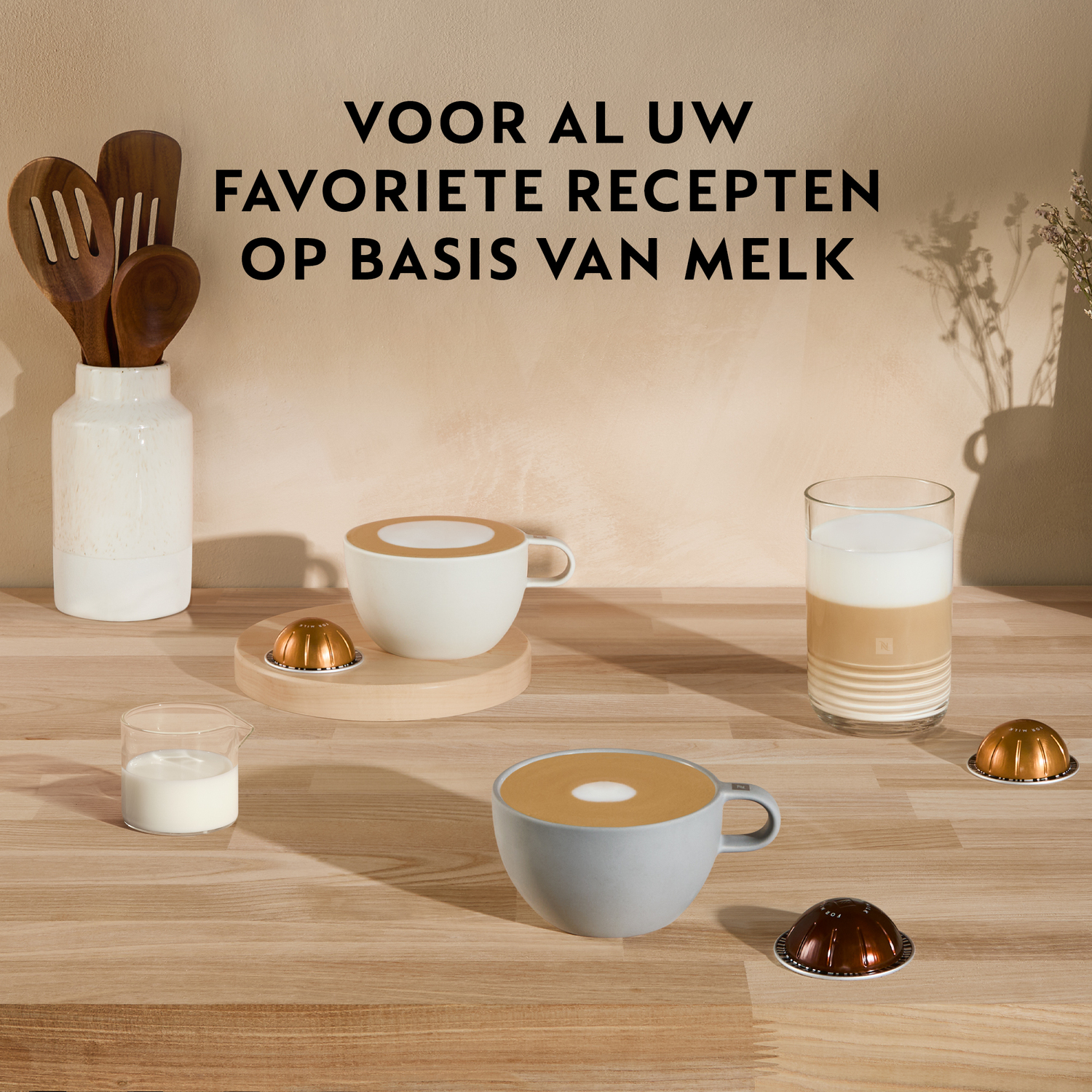 Coffee cups and milk. Milk jug, coffee capsules, wooden spoons, and text on a beige background.