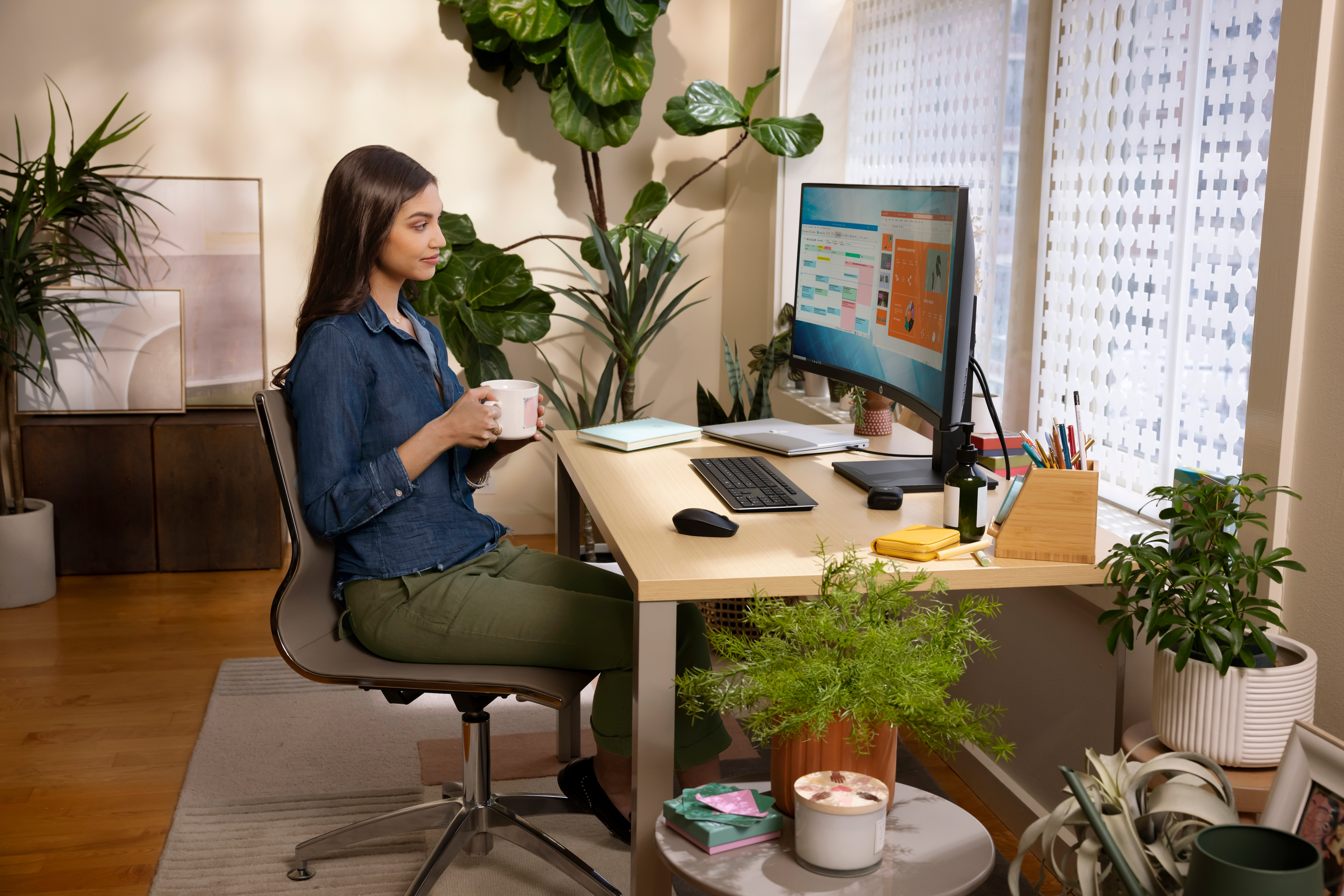 Frau an einem Schreibtisch mit gebogenem Monitor, hält eine Tasse und arbeitet.