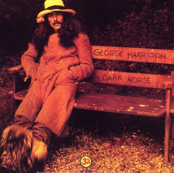 George Harrison auf einer Bank. Dark Horse Albumcover, Brauntöne, Herbstkulisse und ein Hund.