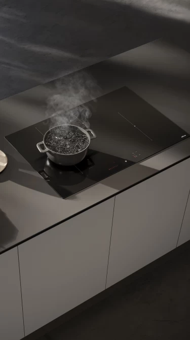 Czarna płyta indukcyjna z garnkiem wrzącej wody na blacie.