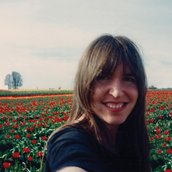 Frau lächelt in einem Feld roter Tulpen, Baum und Himmel im Hintergrund.