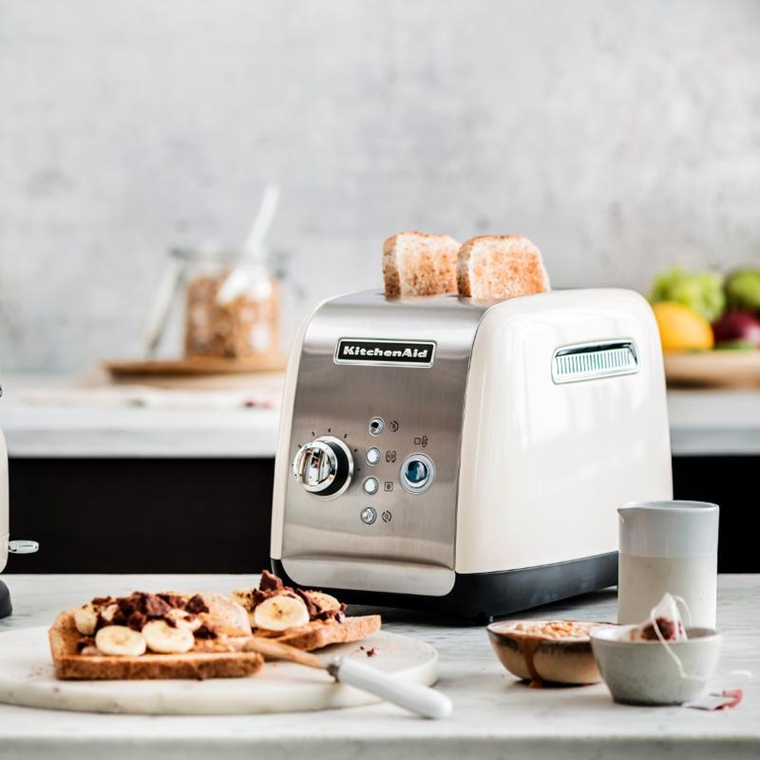 Tostapane KitchenAid con toast. Fette di banana sul toast. Piano cucina bianco. Tè e ciotole.