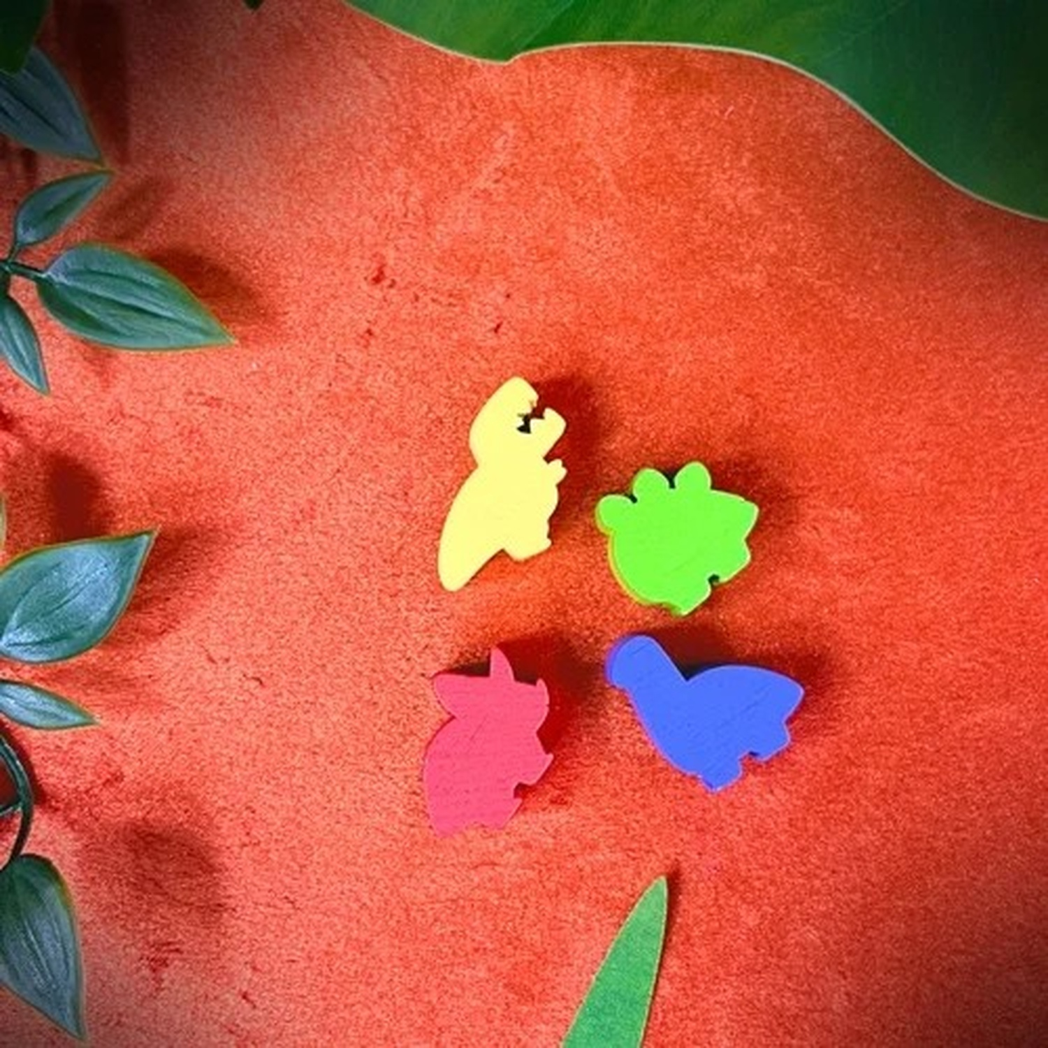 Quattro forme di dinosauri colorati su sfondo rosso, con foglie verdi agli angoli.