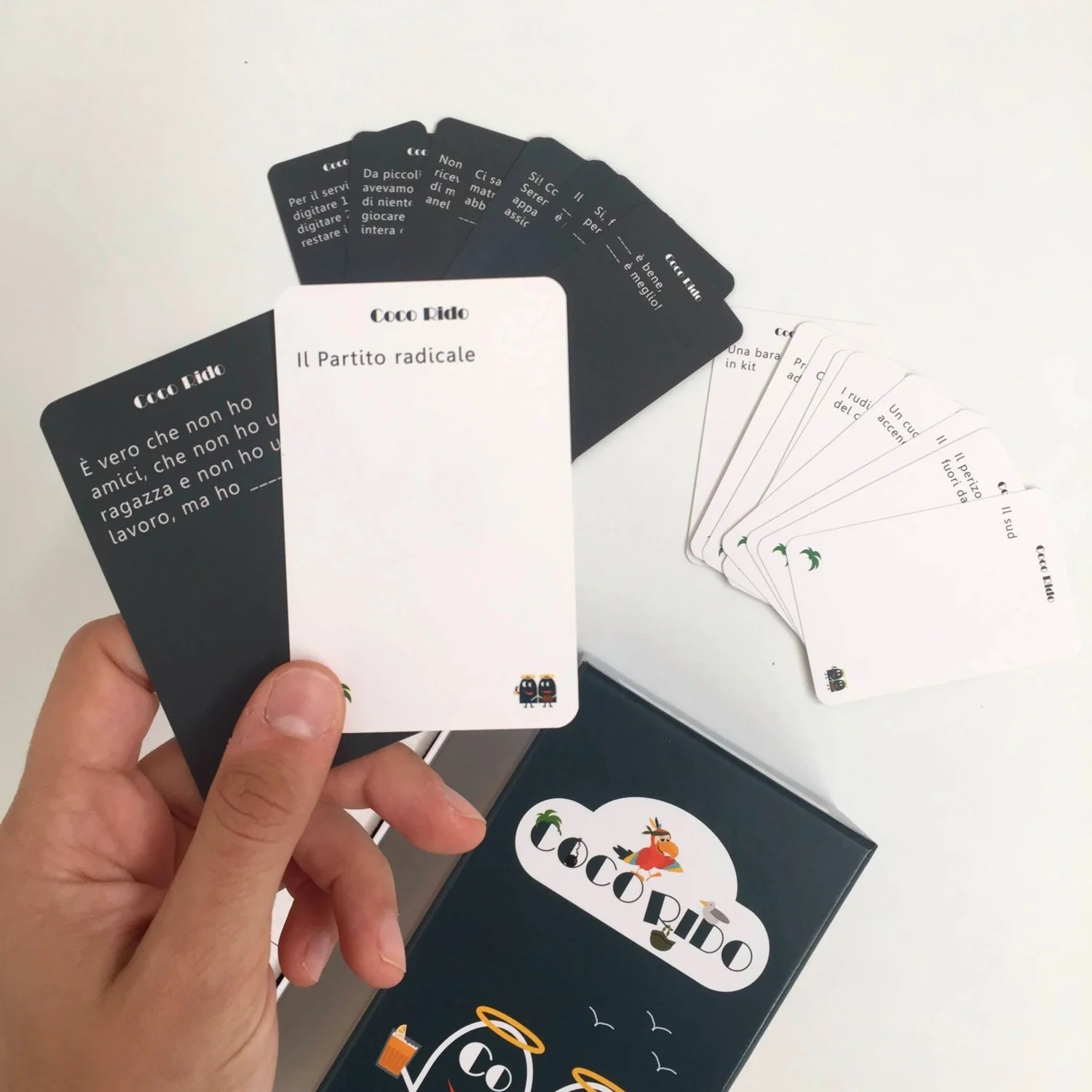 Mano che tiene carte da gioco, bianco e nero, con scatola del gioco sullo sfondo.