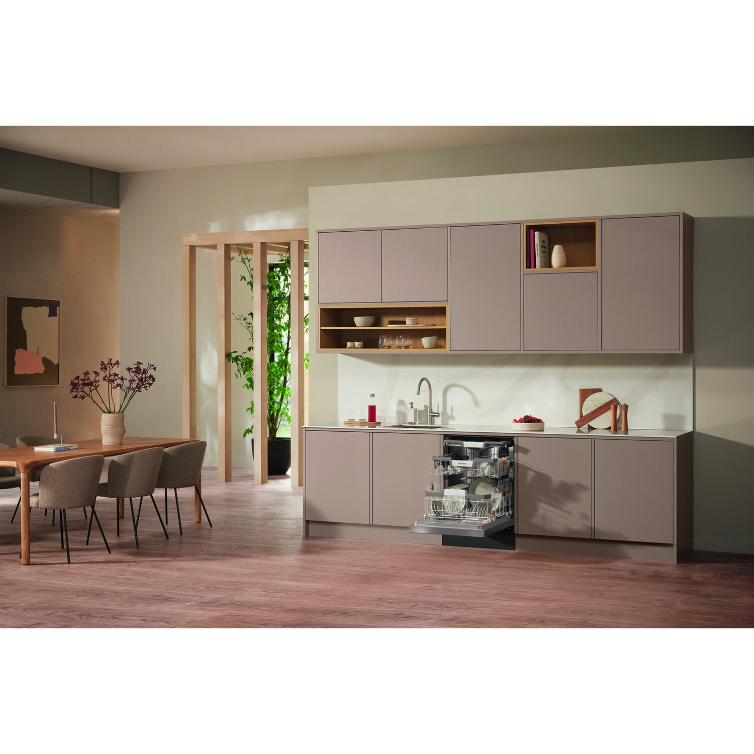 Scena di cucina con lavastoviglie Miele aperta, tavolo da pranzo e mobili da cucina.