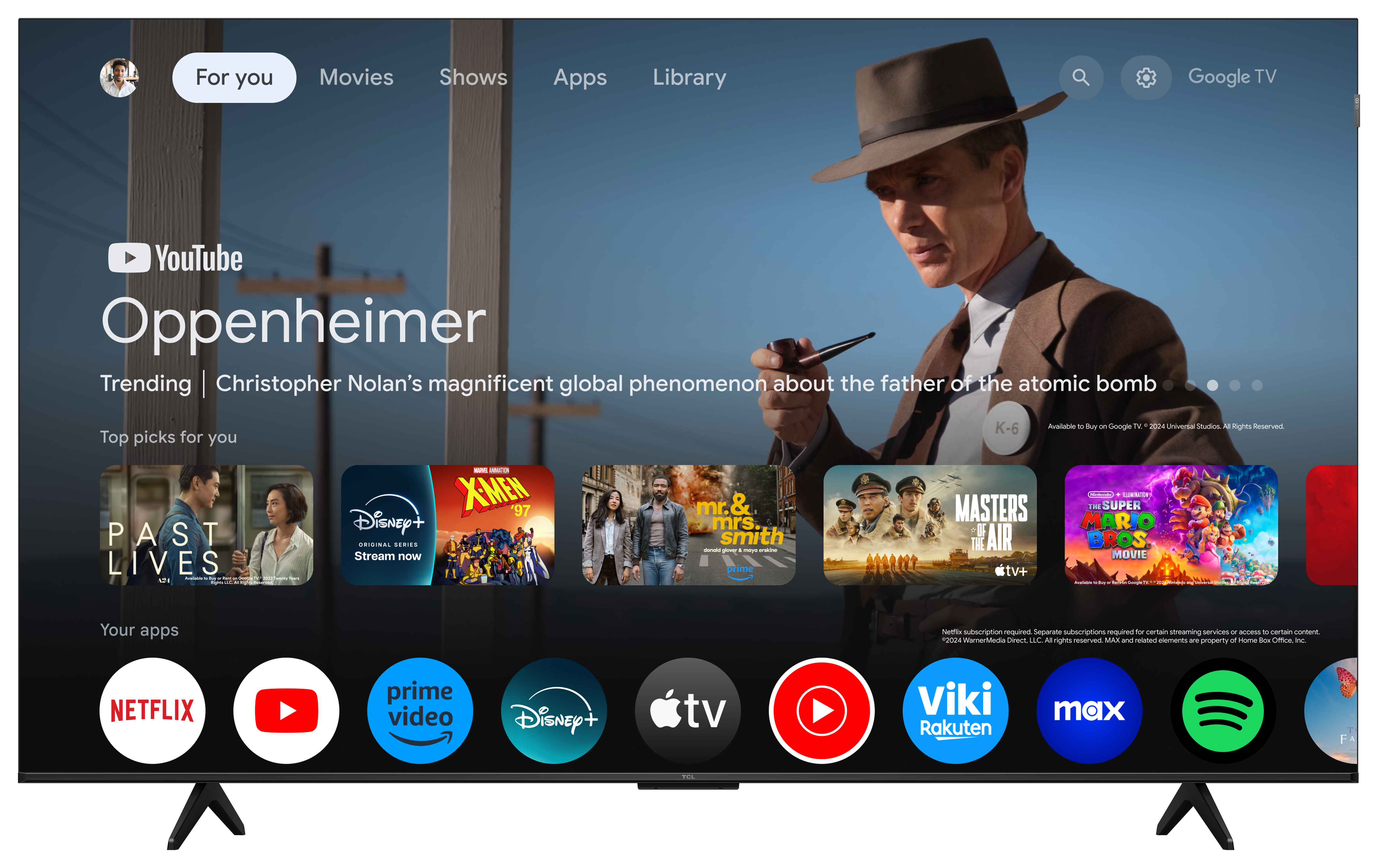 Ekran telewizora wyświetla interfejs Google TV, pokazujący filmy i aplikacje. Mężczyzna w kapeluszu po prawej stronie.