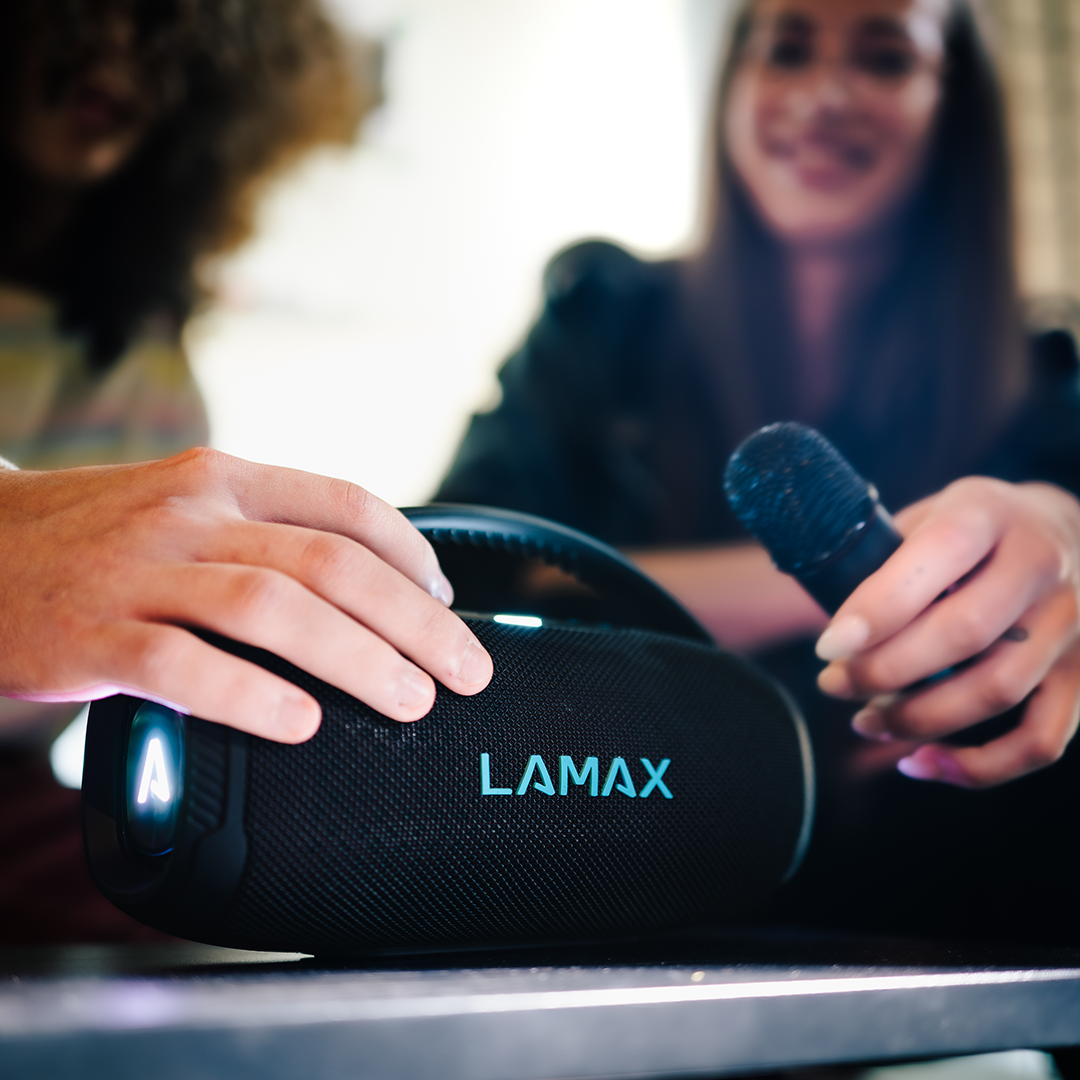Emberek hangszórót és mikrofont használnak. A hangszórón a LAMAX felirat látható.