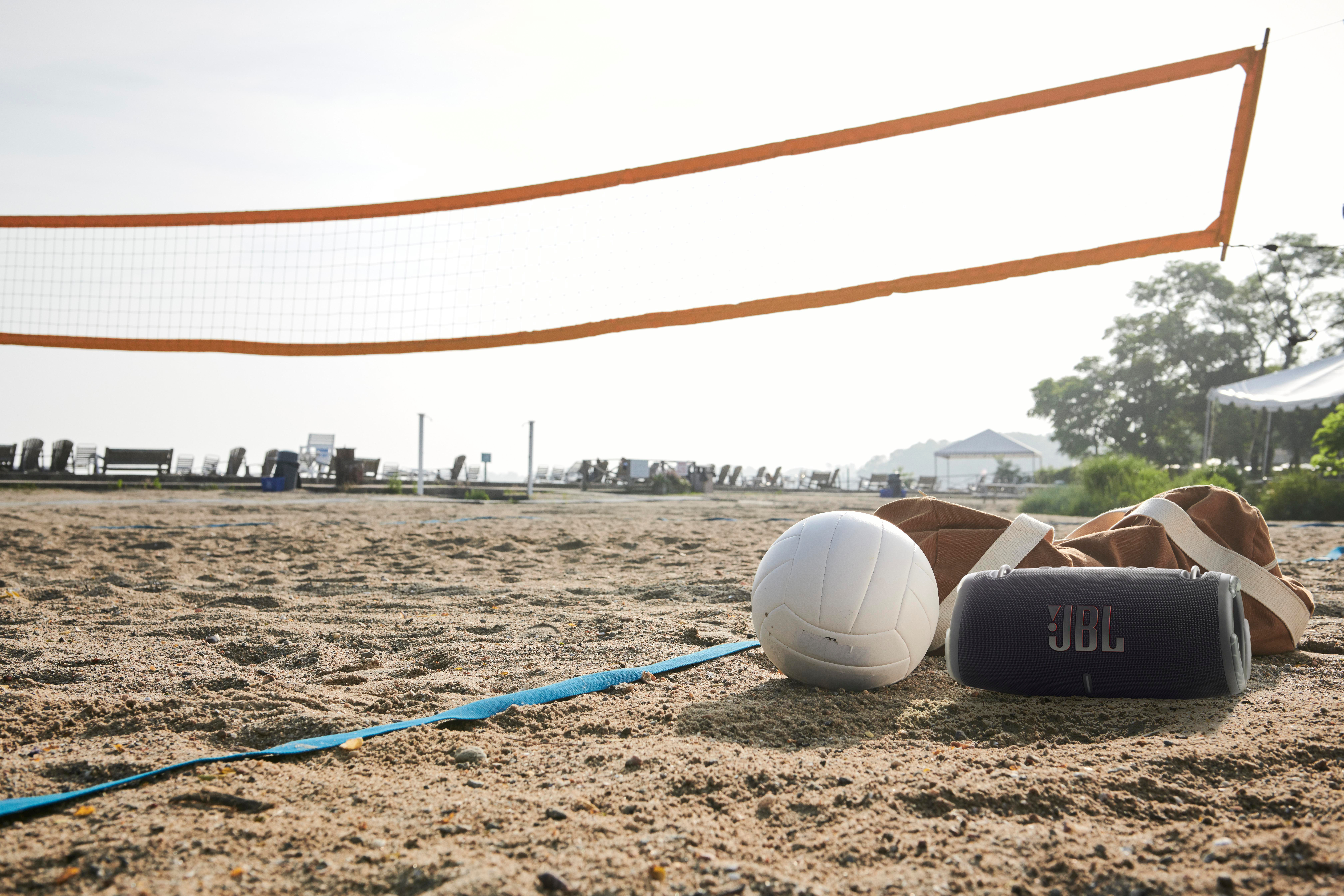 Strandszene mit Volleyballnetz, Ball, Lautsprecher und Hut.