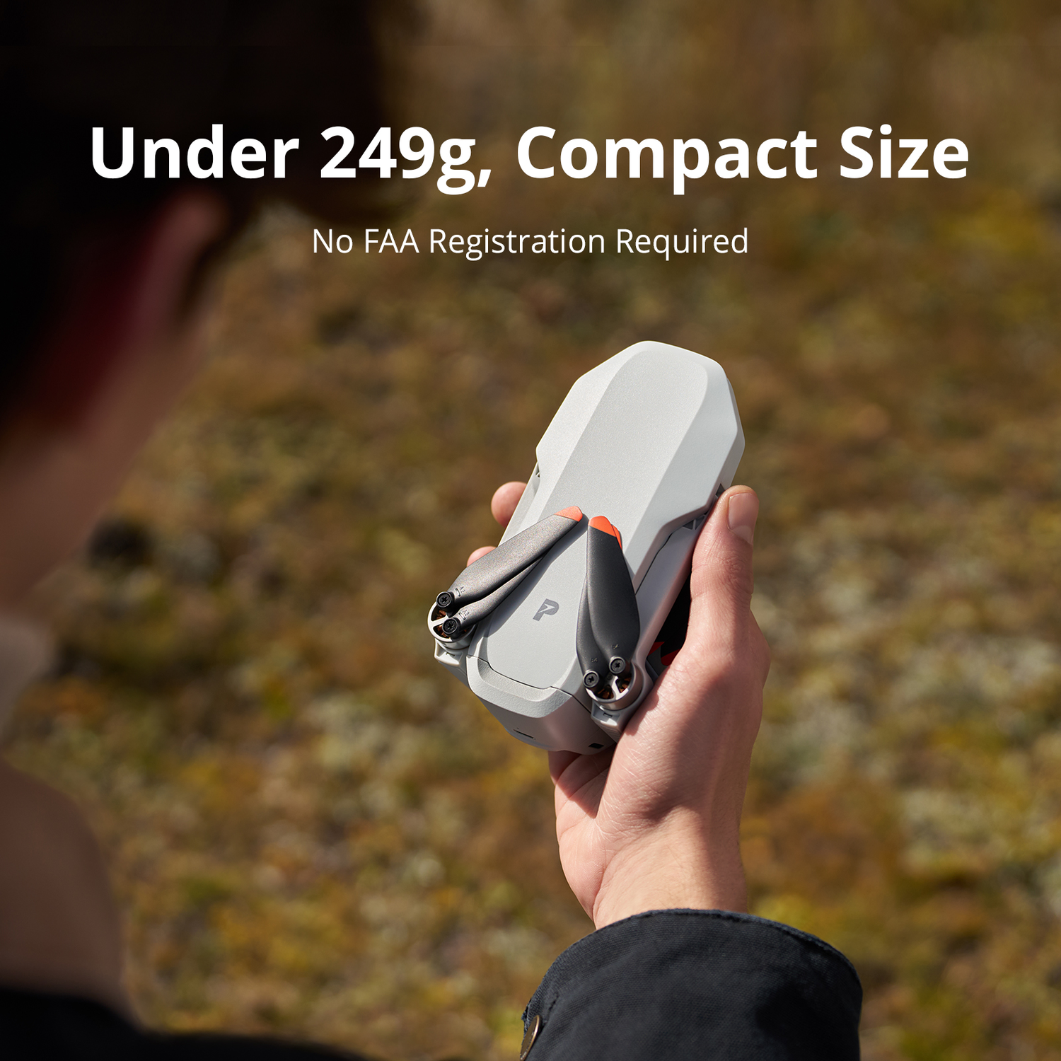 A person holds a folded white drone with black propellers and orange tips.