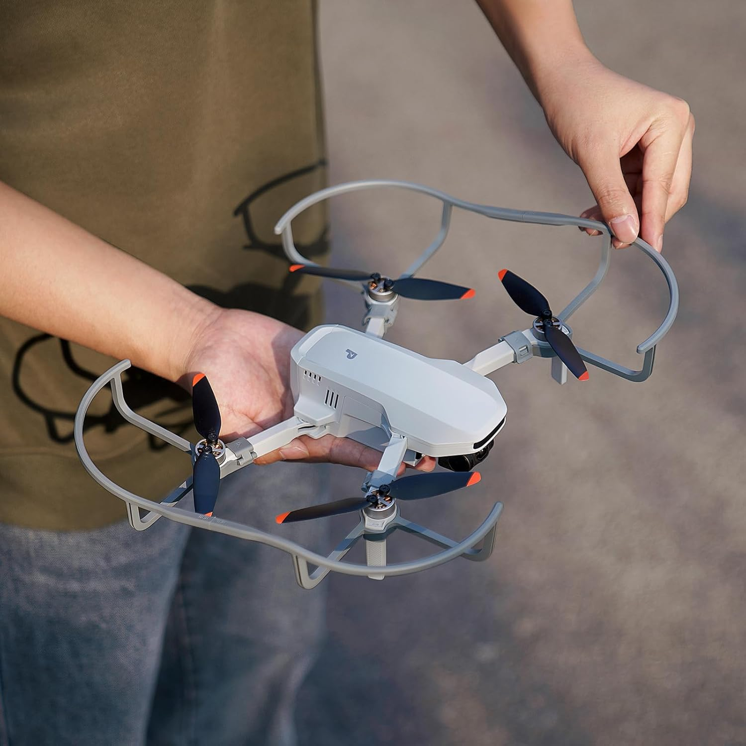 Persoon die een witte drone met zwarte propellers vasthoudt, omringd door grijze beschermers.