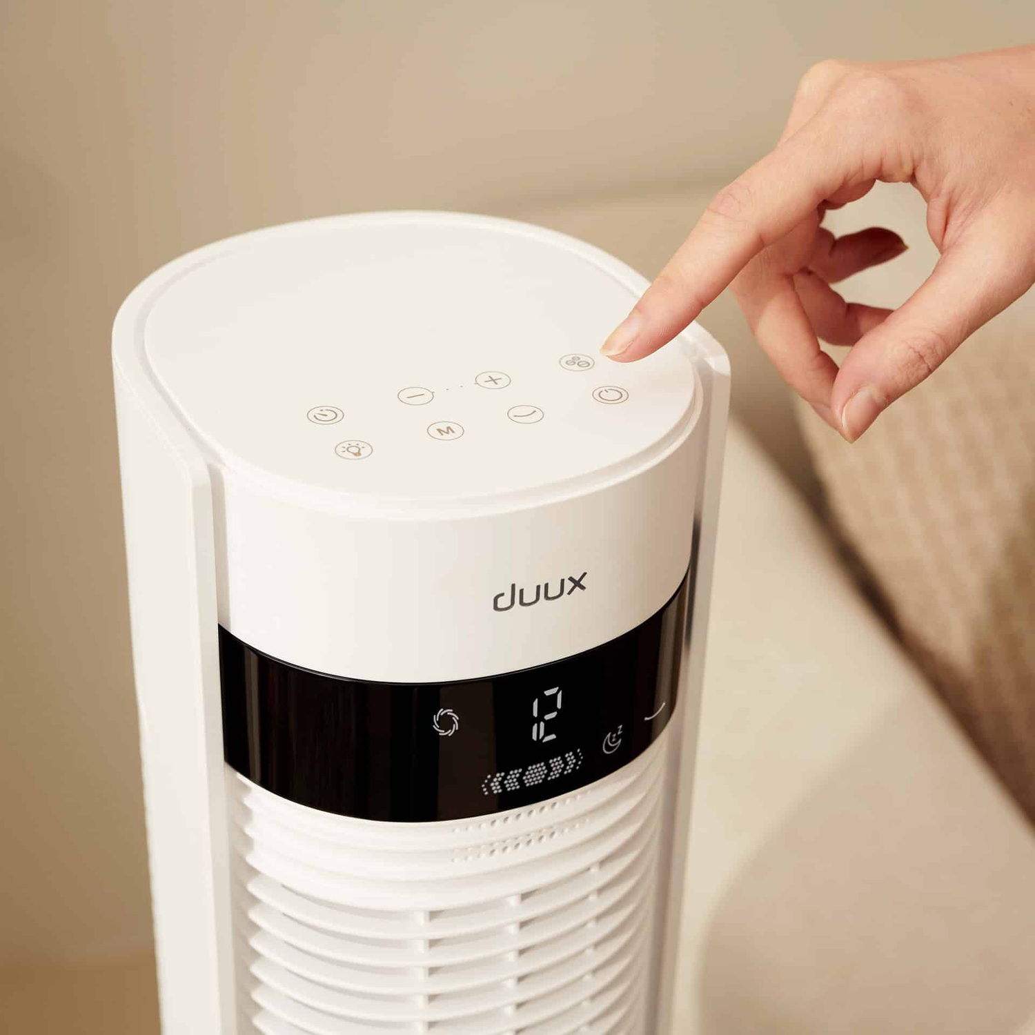 Een hand die op een knop bovenop een torenventilator drukt. Het display van de ventilator toont een nummer.