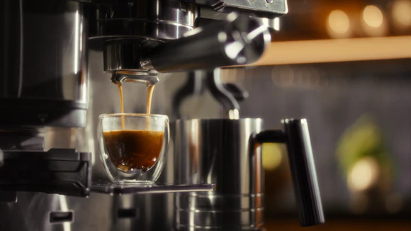 Bir kahve makinesinin bir bardak bardağa espresso döktüğünün yakın çekimi.