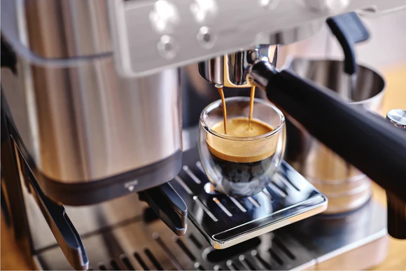 Bir kahve makinesinin bir bardak bardağa espresso döktüğünün yakın çekimi.