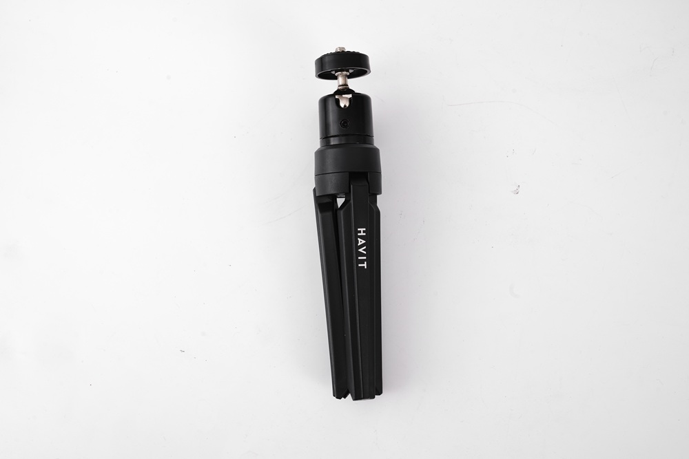 Katlanmış bacaklı siyah tripod, HAVIT markası, beyaz zemin üzerinde.