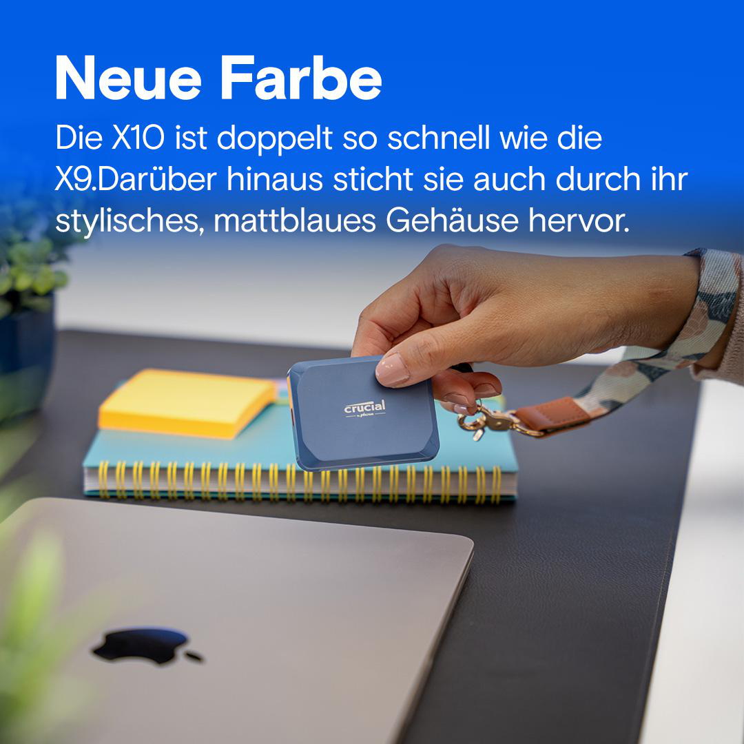 Eine Hand hält eine blaue Crucial SSD über einem Laptop und Notizbüchern auf einem Schreibtisch.