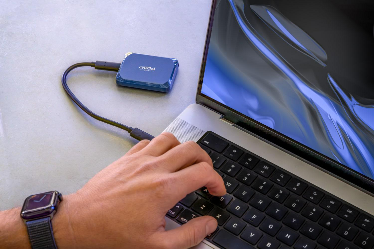 Die Hand einer Person tippt auf einer Laptop-Tastatur, daneben eine blaue Crucial SSD.