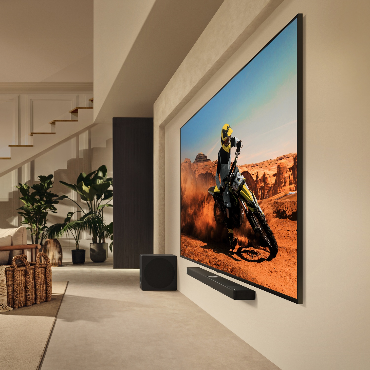 TV su un muro, con una persona in moto sullo schermo, una soundbar e un subwoofer.