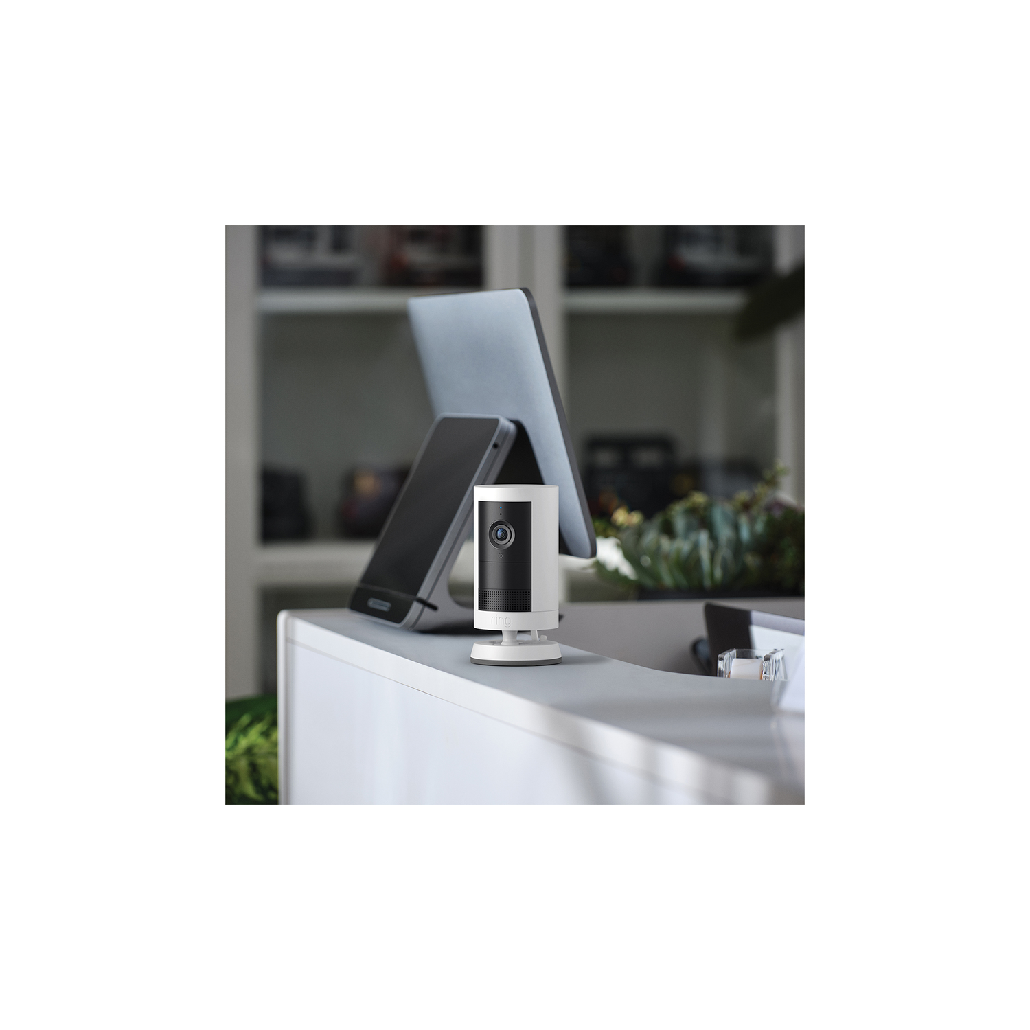 White security camera on a white surface. Laptop and phone behind.