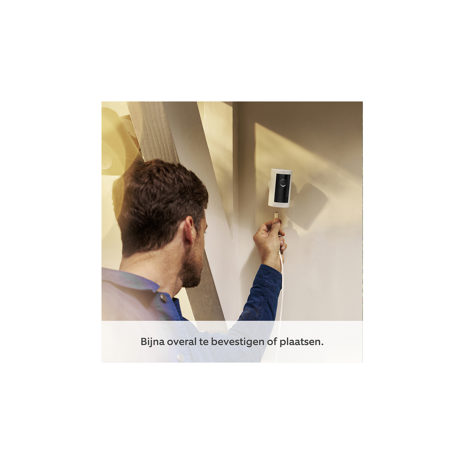 Man installing a white security camera on a wall. White cable visible.