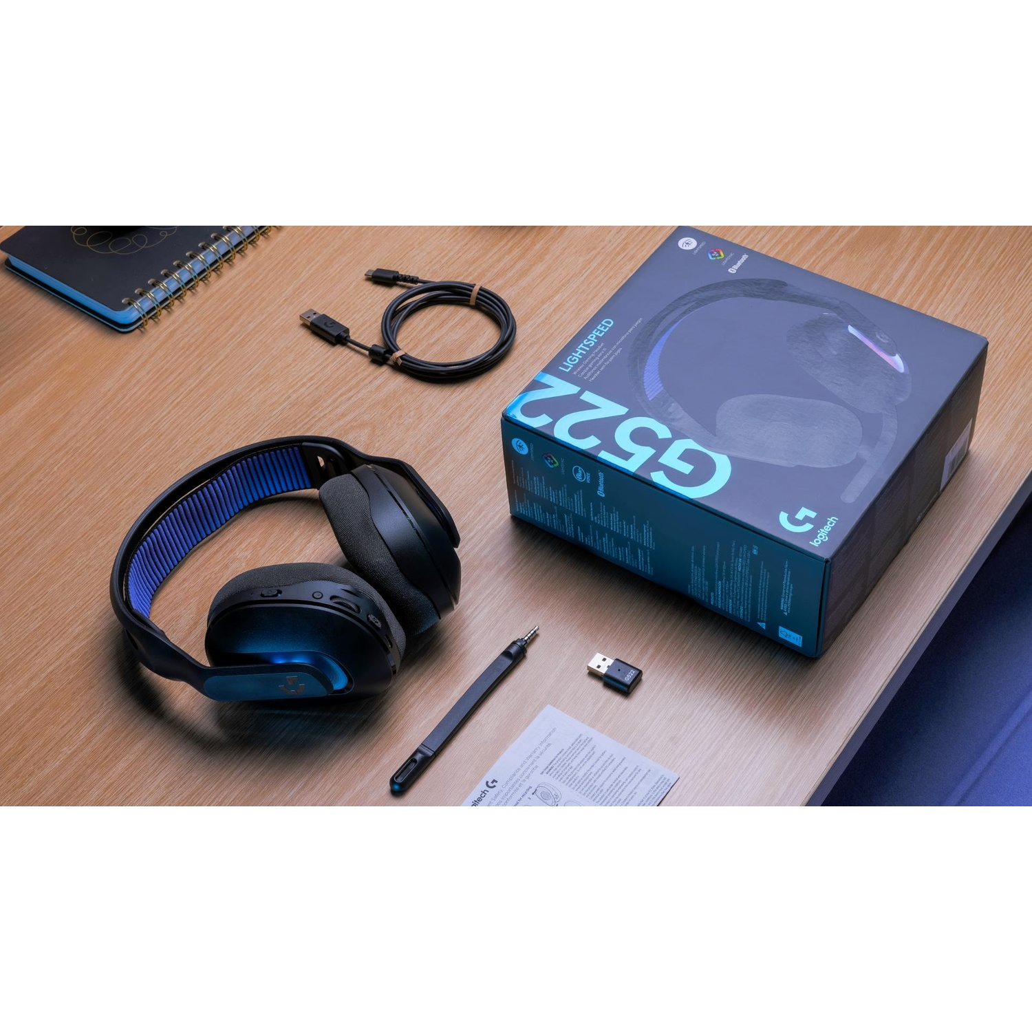 Configurazione scrivania con cuffie, scatola e accessori. Sono visibili un cavo, un dongle e una penna.