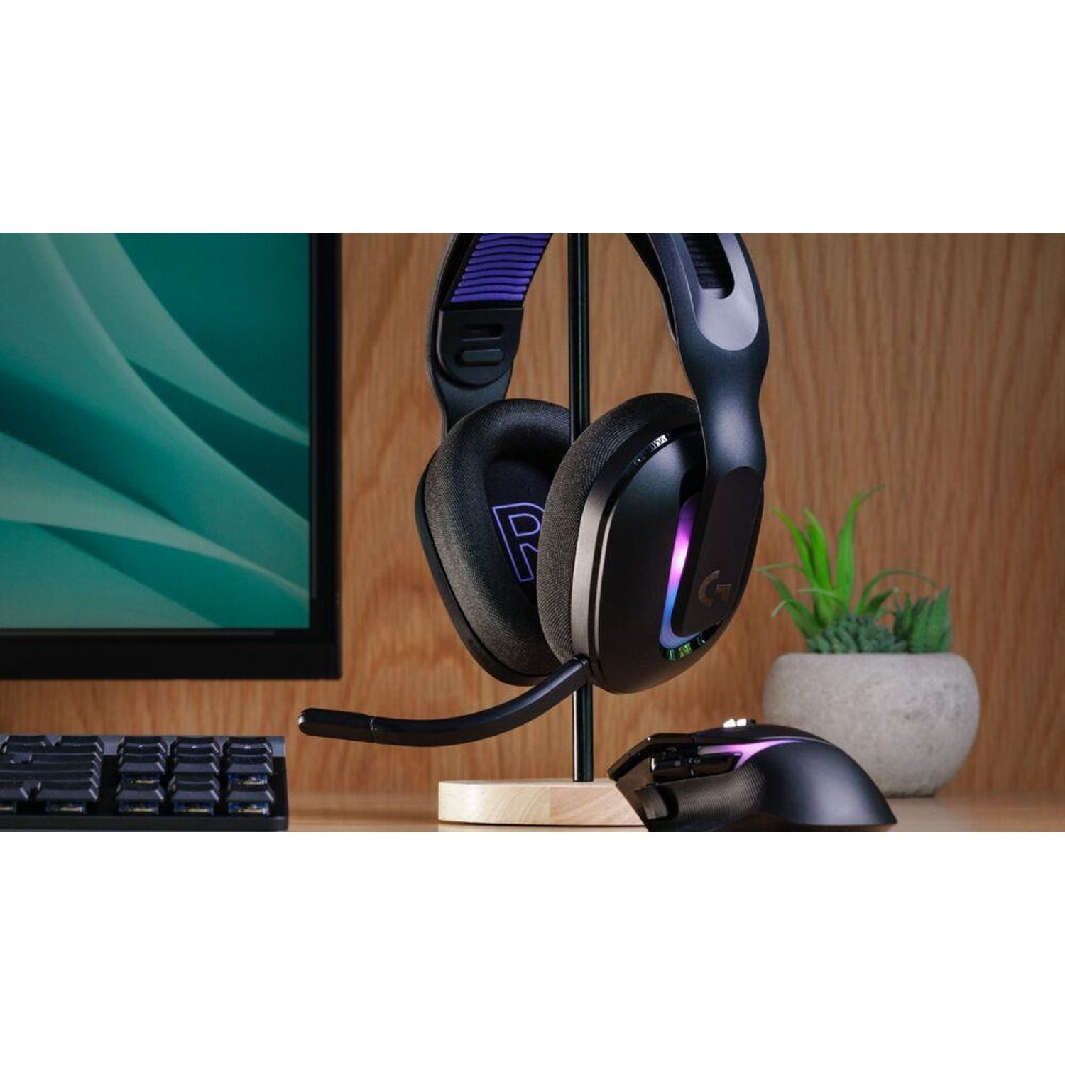 Cuffie da gioco nere su supporto, mouse e tastiera su scrivania con monitor e piccola pianta.