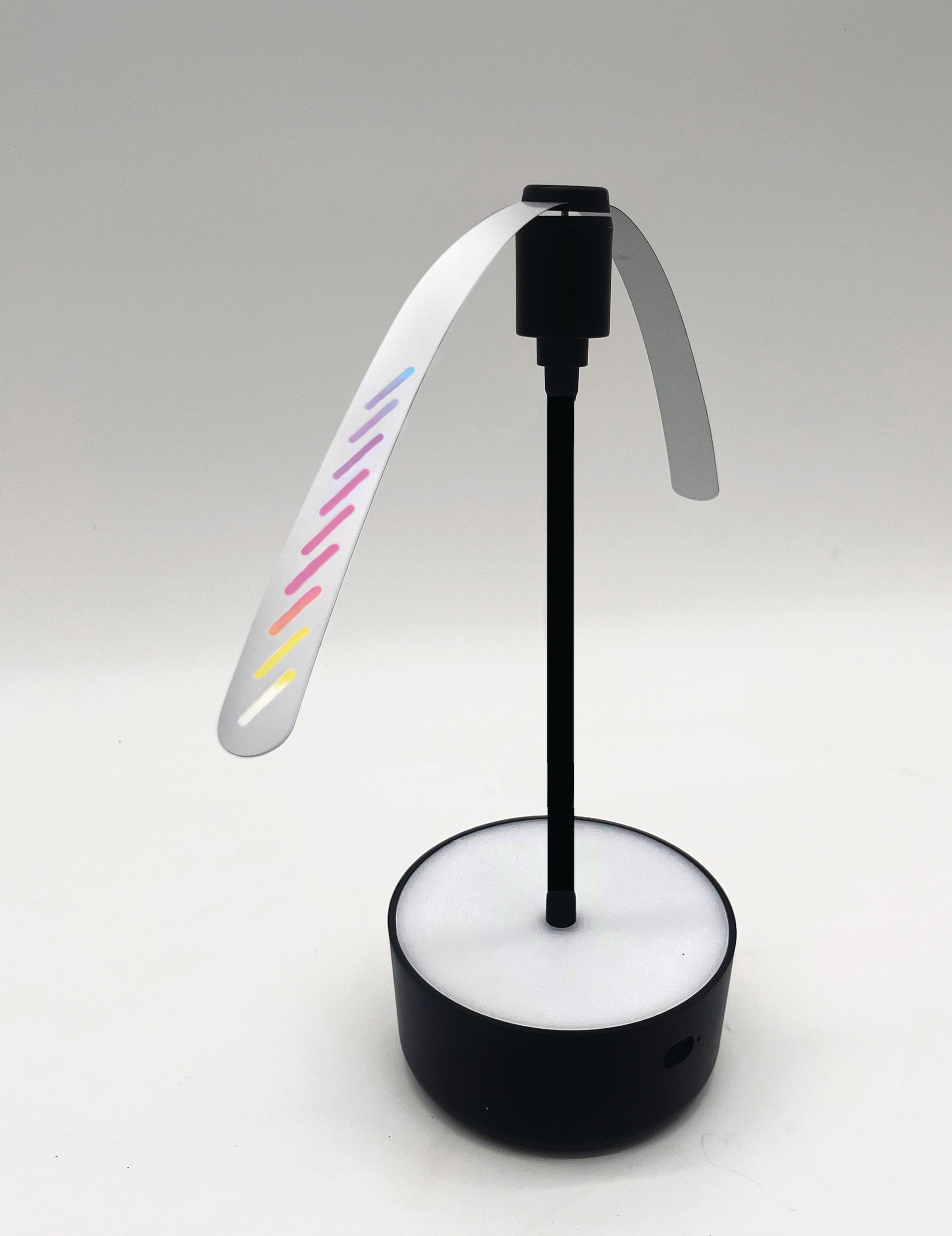 Schwarze Lampe mit einem weißen, gebogenen Teil und bunten Lichtern auf weißer Basis.