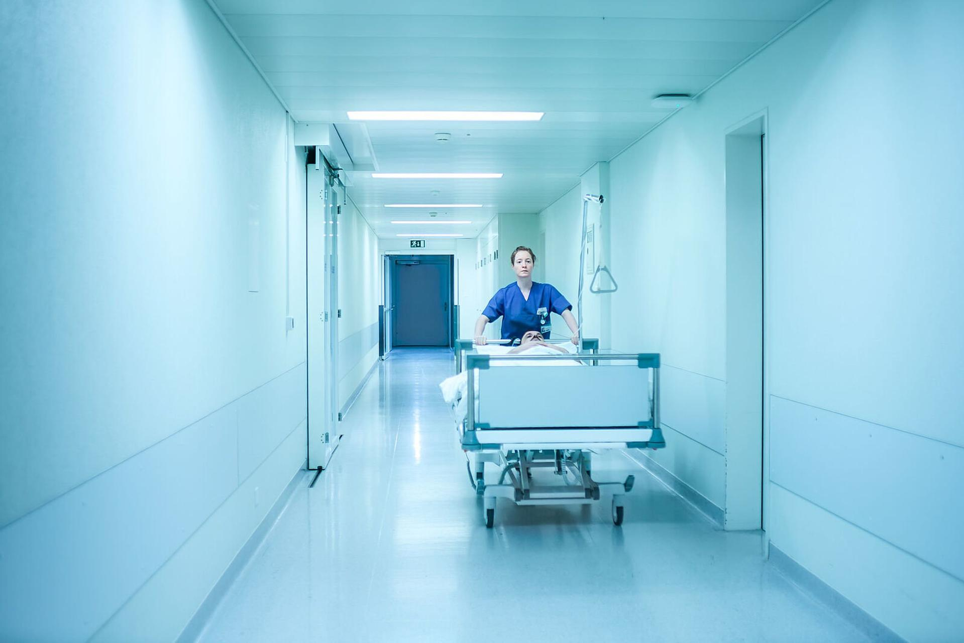 Krankenschwester schiebt ein Bett einen hellen Krankenhausflur entlang.