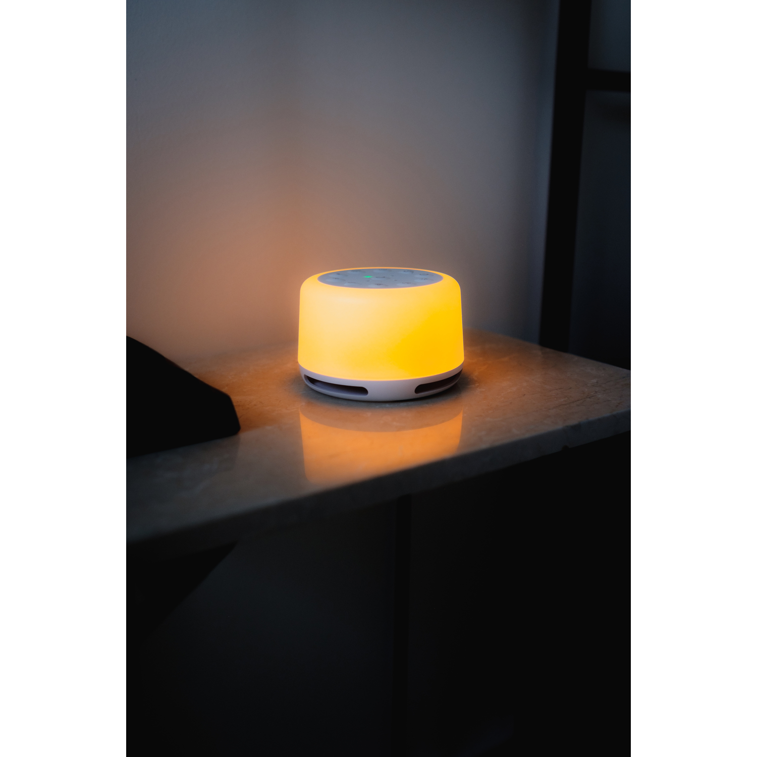 A white and yellow glowing sound machine on a marble-like table, dark background.