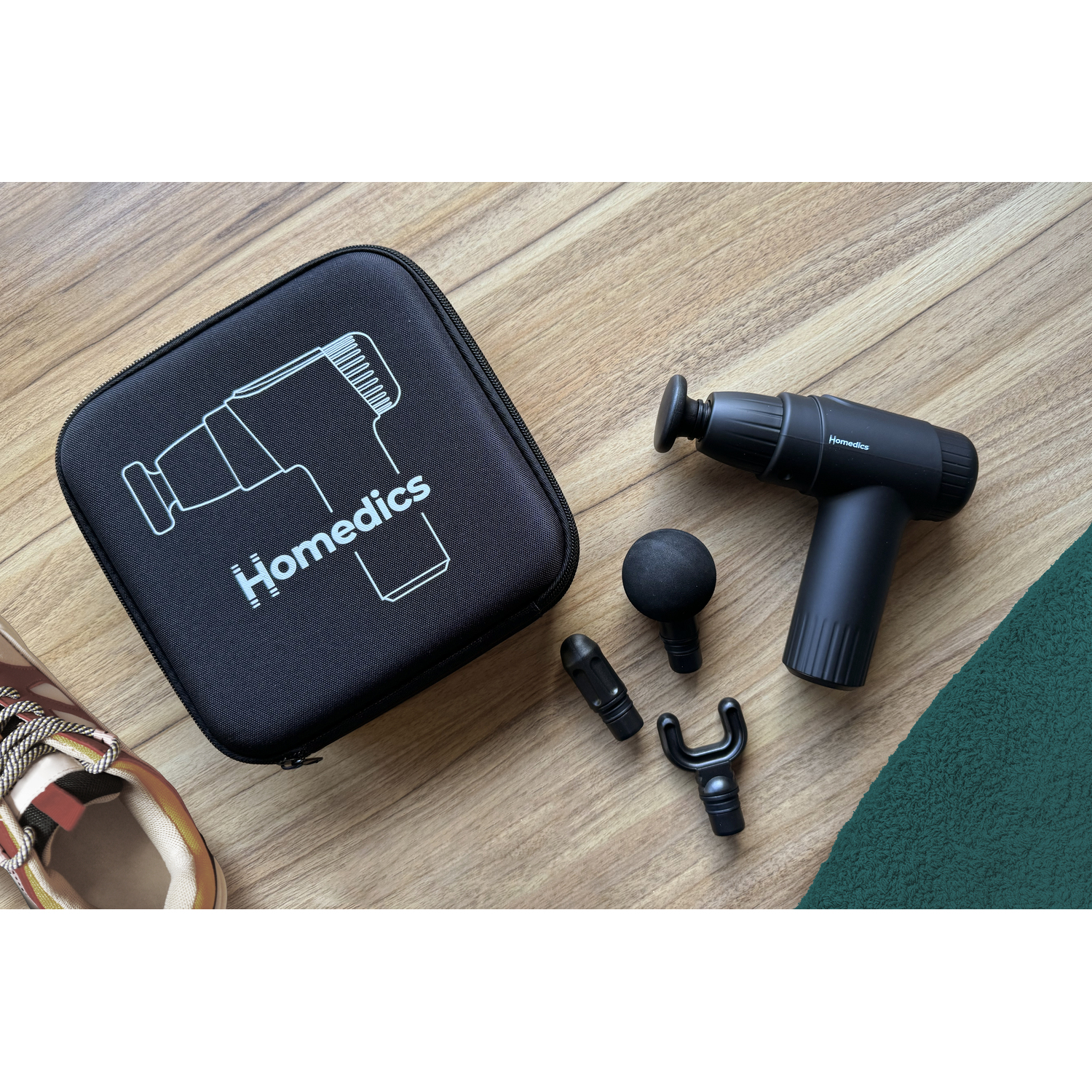 A black massage gun and attachments are on a wooden surface next to a carrying case.