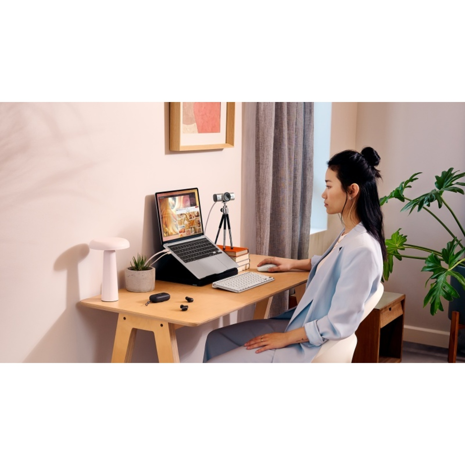 A woman is sitting at a desk with a laptop and webcam.
