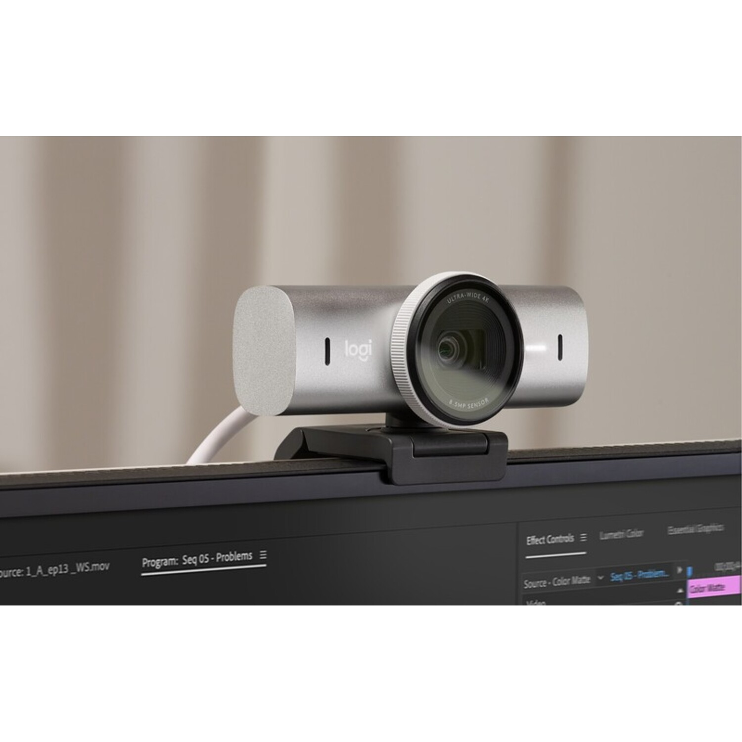 A silver webcam sits on a monitor, with a black stand. The monitor displays a video editing interface.