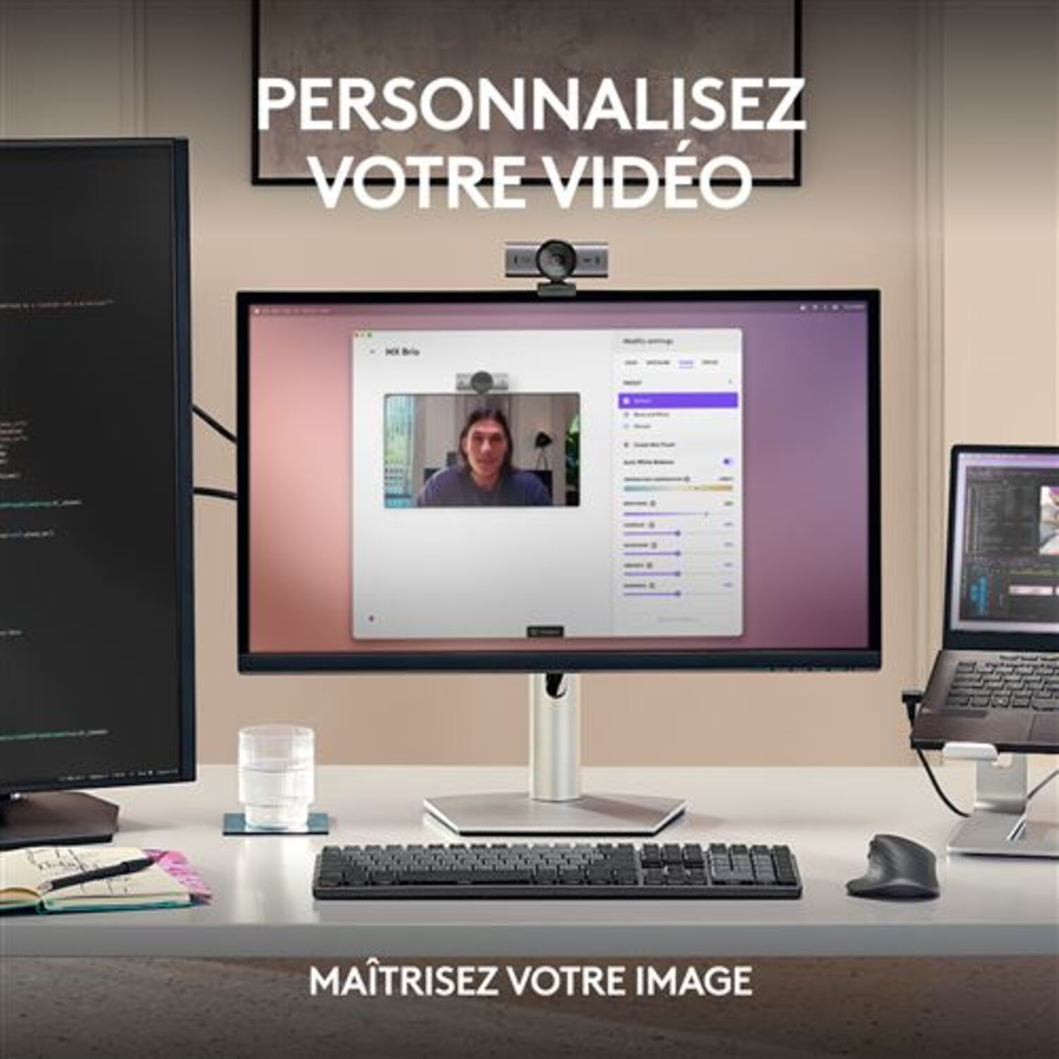 Un bureau avec une webcam sur un moniteur, clavier, souris et ordinateur portable. Une personne est sur le moniteur.