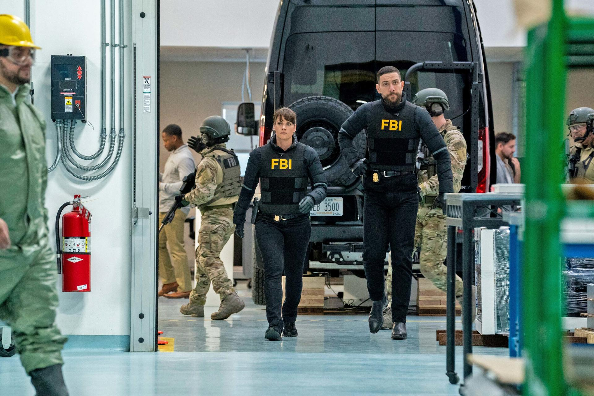 FBI-Agenten gehen durch eine Einrichtung. Andere stehen in der Nähe. Ein Feuerlöscher und ein Transporter sind sichtbar.