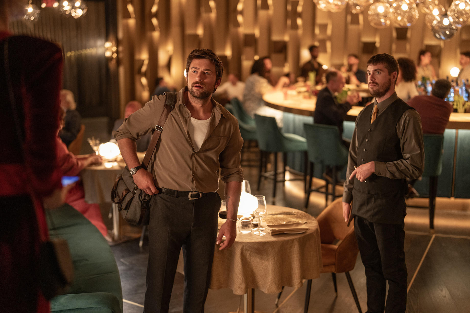 Zwei Männer und eine Frau in einem Restaurant. Der Mann in der Mitte schaut weg.