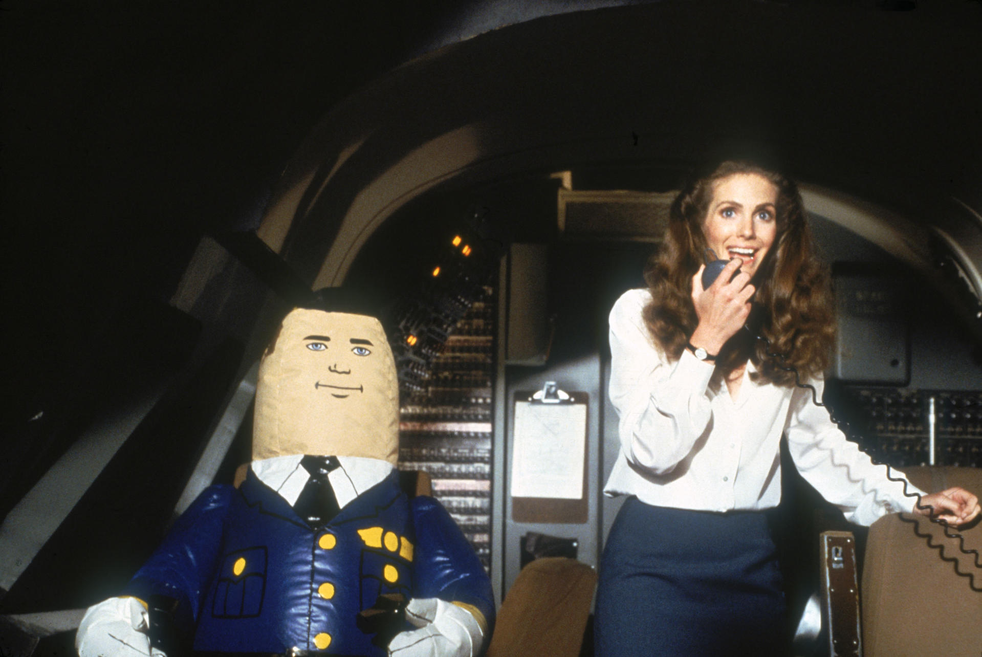 Eine Frau spricht über Funk, während ein Maskottchen neben ihr in einem Cockpit steht.