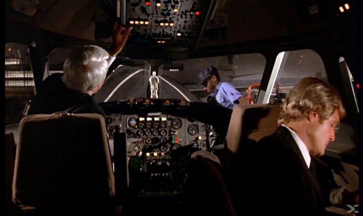 In einem Flugzeugcockpit sind zwei Männer anwesend, einer schaut auf die Instrumente.