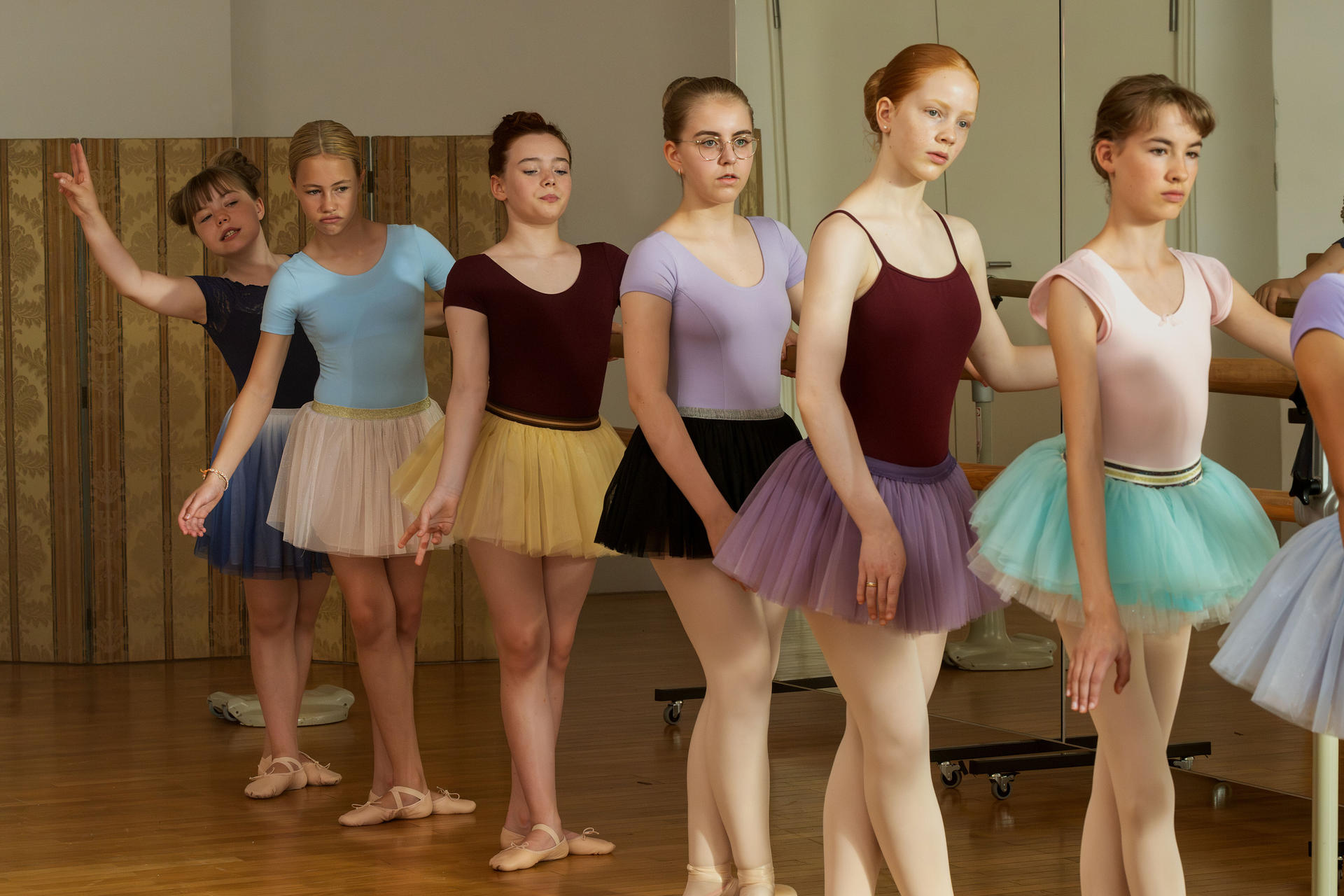 Ballettunterricht. Sieben junge Ballerinas in Tutus stehen an einer Stange und üben Posen.