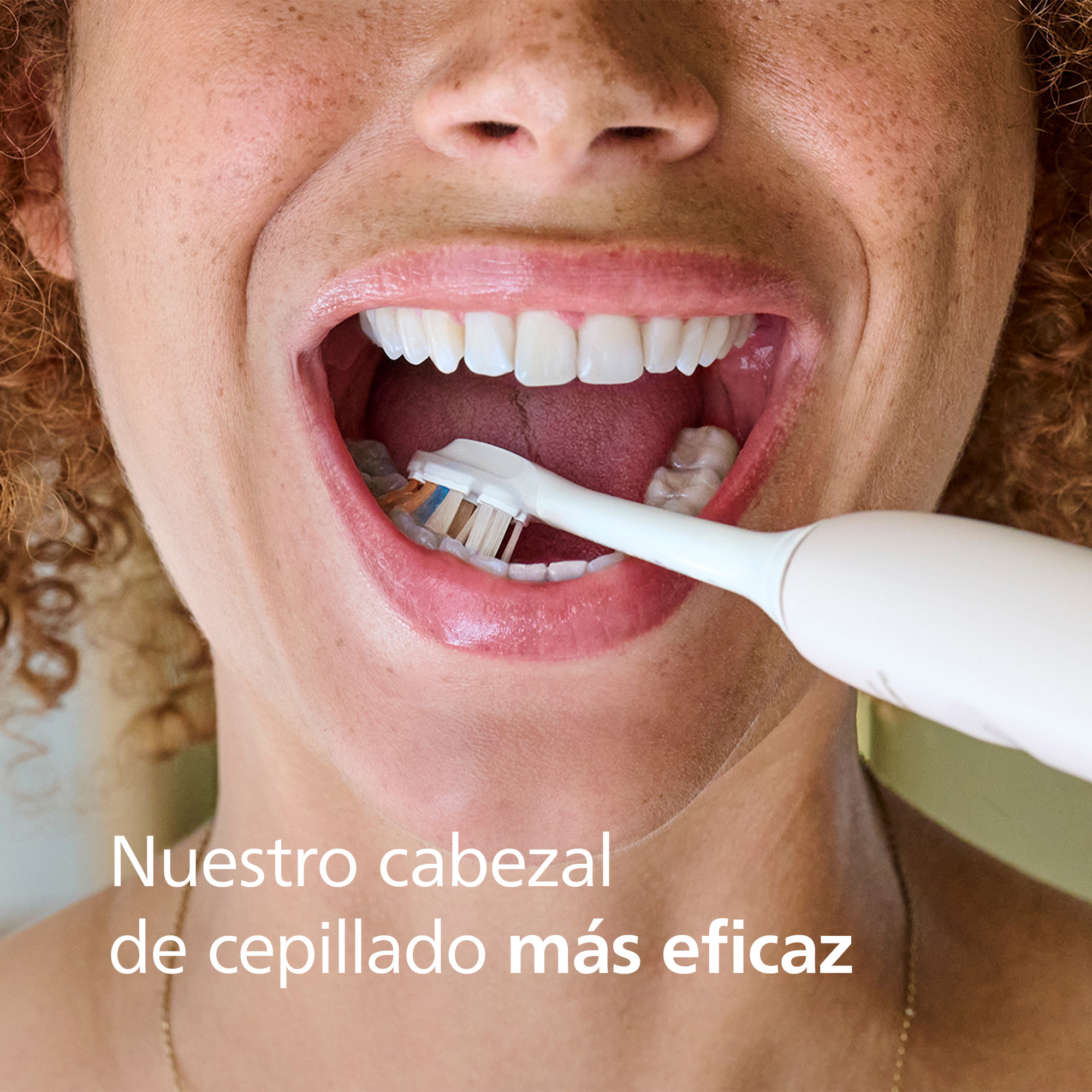 Una mujer sonríe, usando un cepillo de dientes en su boca. El texto dice: 'Nuestro cabezal más eficaz'.