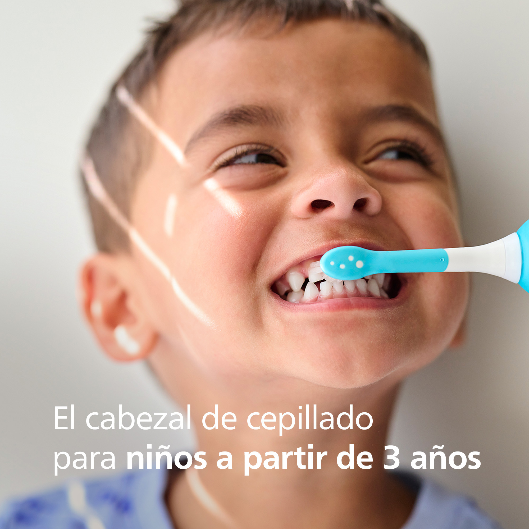 Un niño pequeño sonríe mientras un cepillo de dientes azul le limpia los dientes. El cepillo está en su boca.