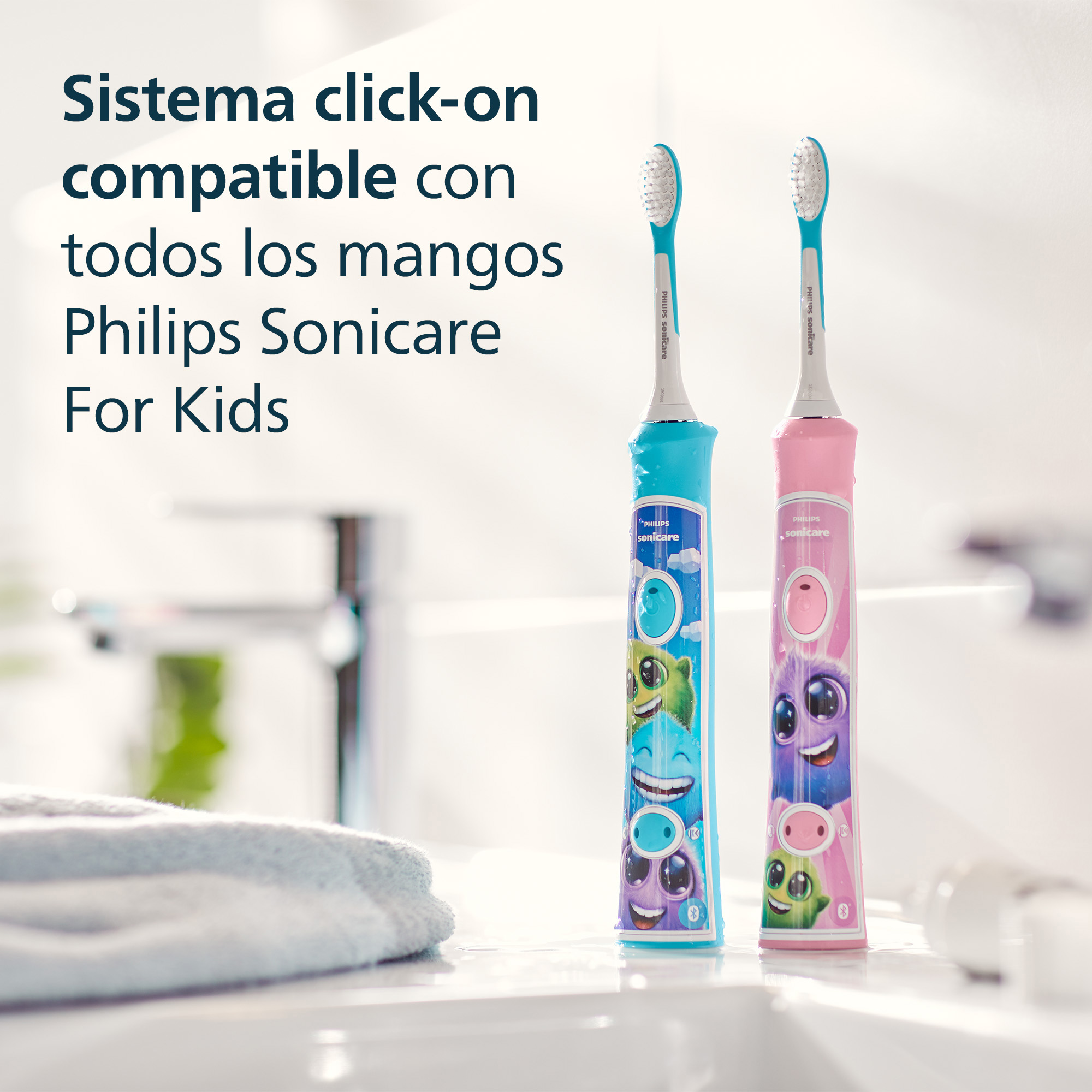 Dos cepillos de dientes para niños, azul y rosa, están sobre una encimera. Una toalla y un espejo están en el fondo.