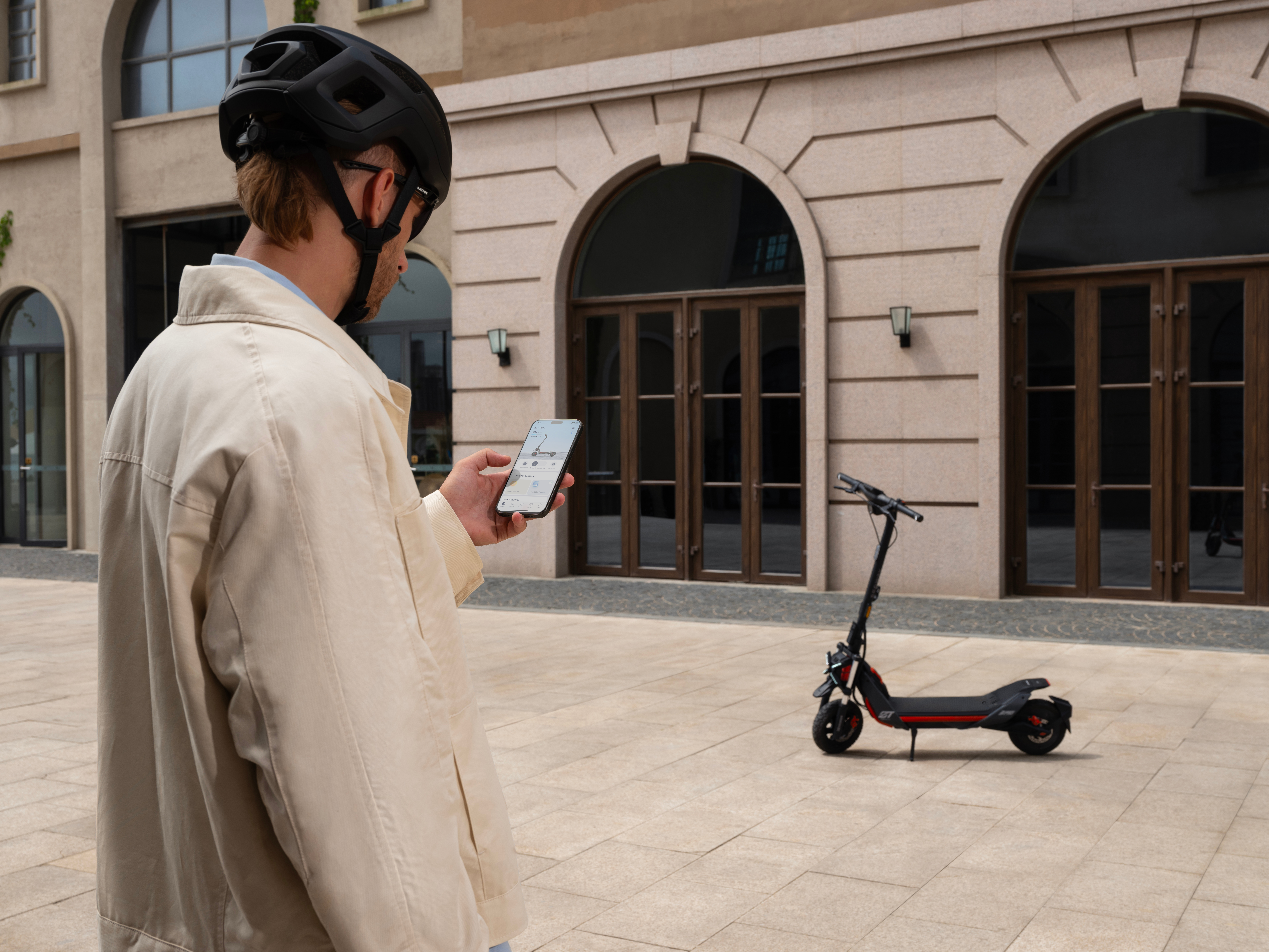 Kasklı bir adam, bir scooterın yanında telefonunu kontrol ediyor.