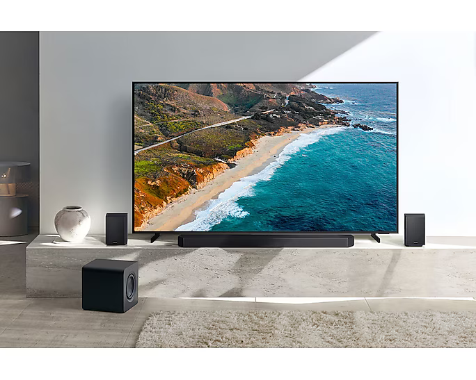 Egy nappali berendezése TV-vel, soundbarral, hangszórókkal és mélynyomóval. A TV egy tengerparti jelenetet jelenít meg.