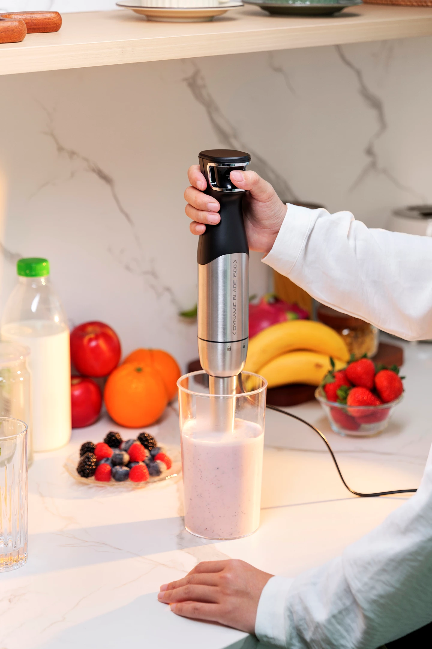 Person mixt einen rosa Smoothie in einem Glas mit einem Mixer, in einer Küchenumgebung.