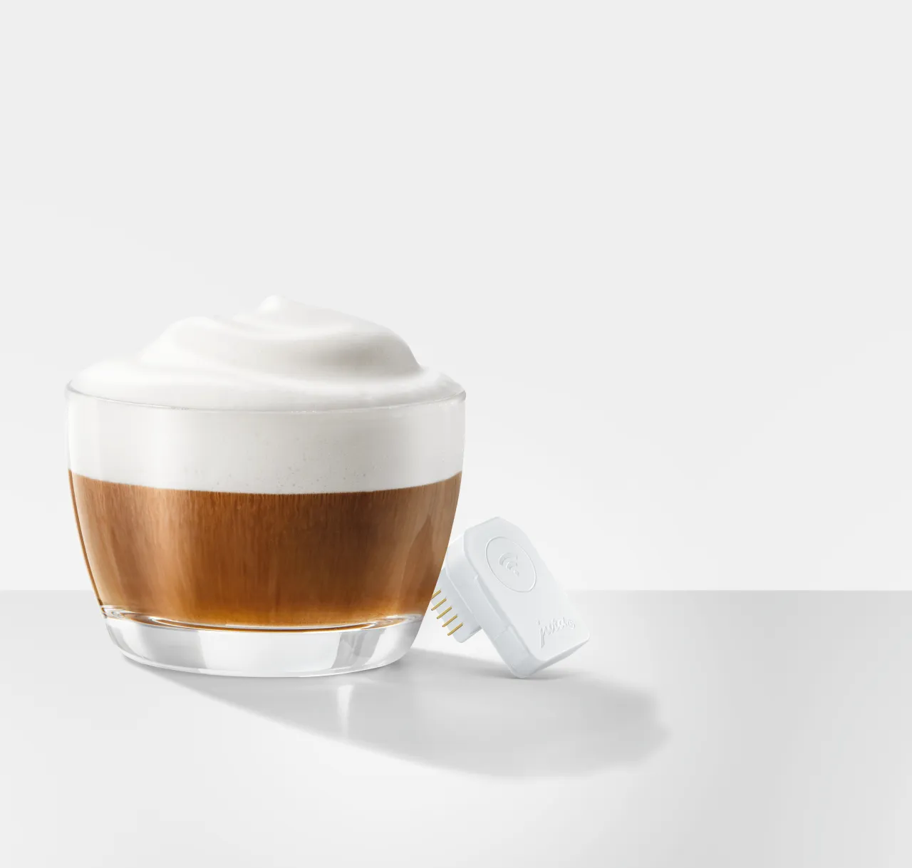 Bicchiere di caffè con schiuma e una spina intelligente bianca accanto.