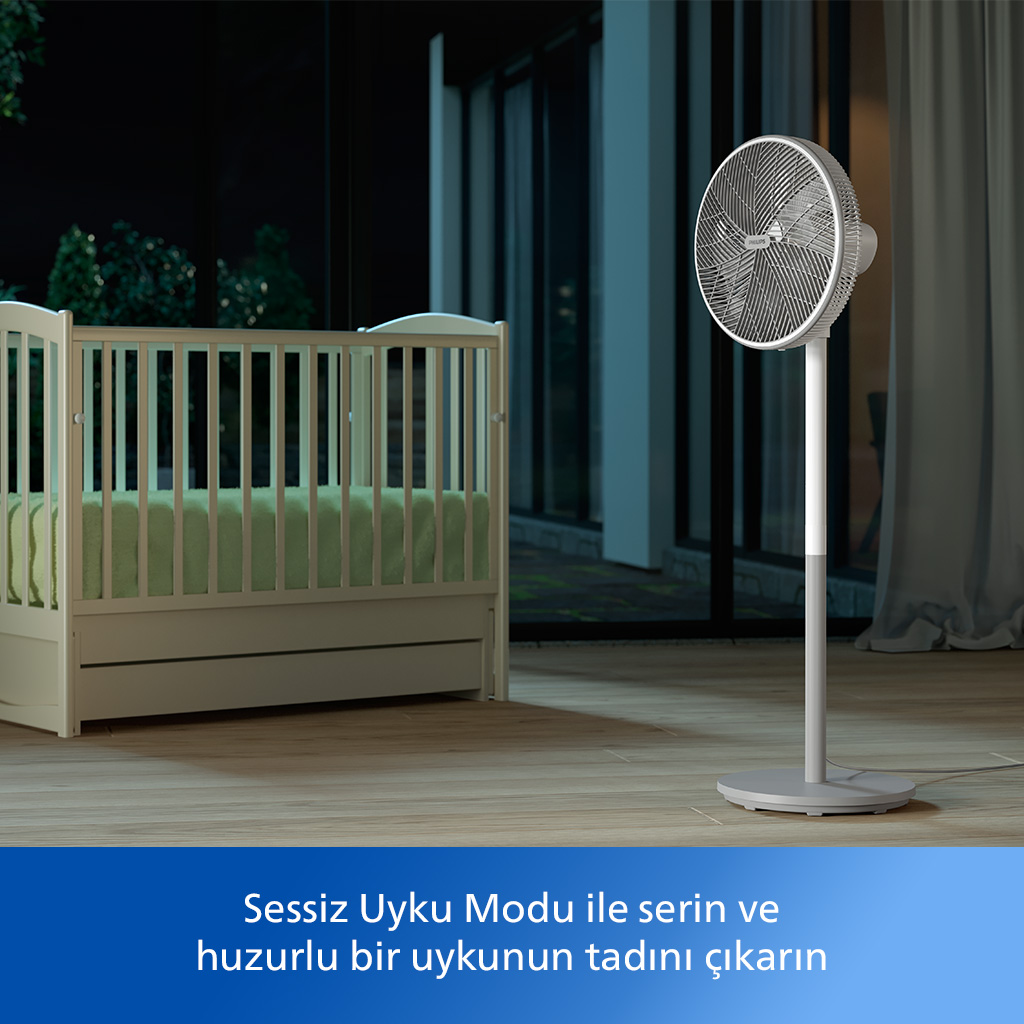 Gece bir beşik bulunan odada beyaz vantilatör. Ahşap zemin, beyaz perdeler ve bir pencere.