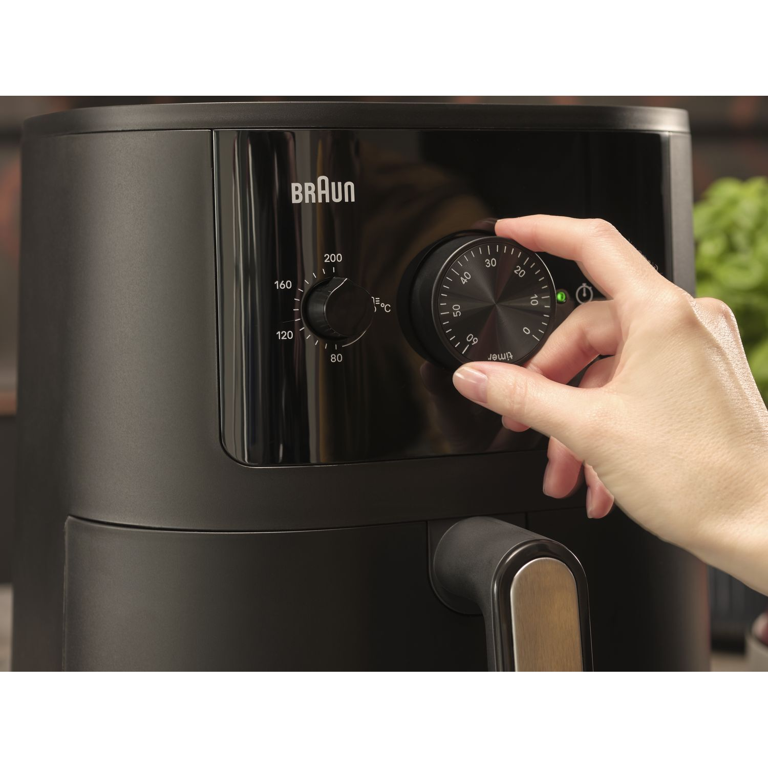 Hand die de timerknop van een zwarte airfryer aanpast, merk Braun.