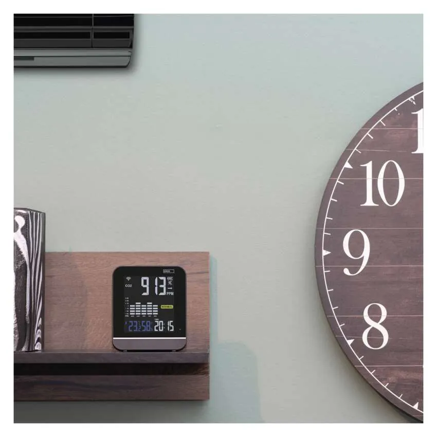 CO2 monitor egy fa polcon. Egy nagy óra a háttérben.