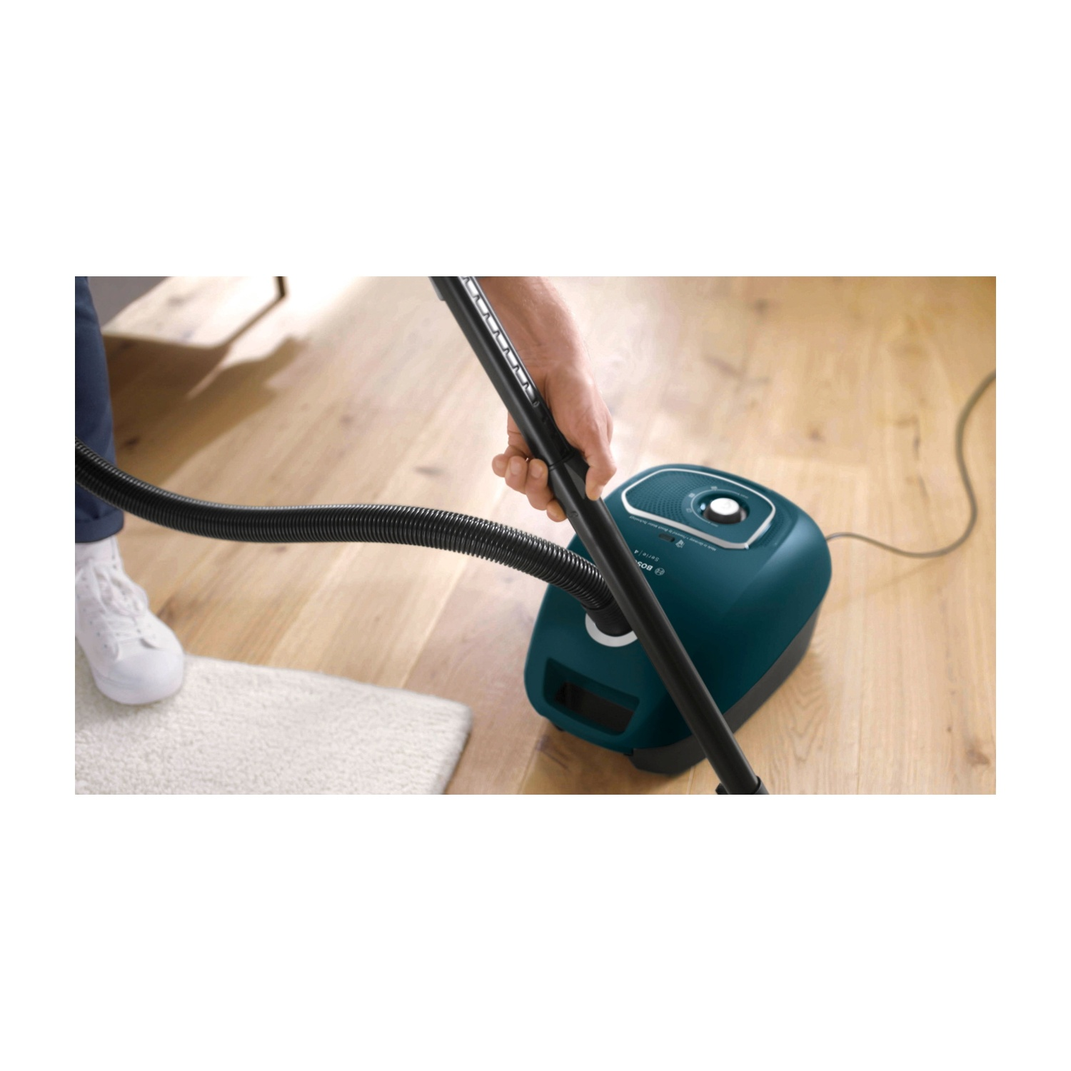 Persona che mette un aspirapolvere Bosch verde acqua in un mobile di legno. Vengono mostrate immagini aggiuntive.