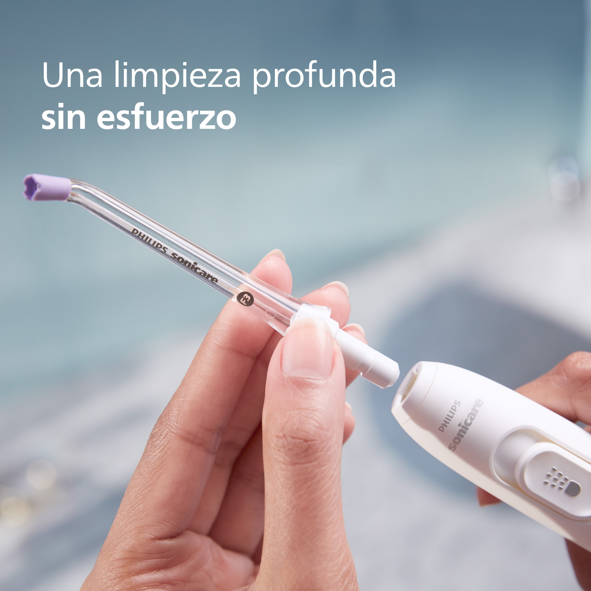 Manos de una persona usando un irrigador oral Philips Sonicare, con la boquilla insertada.