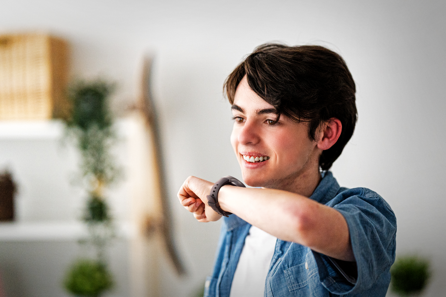 Un chico sonriente mira su reloj inteligente. Un fondo claro.